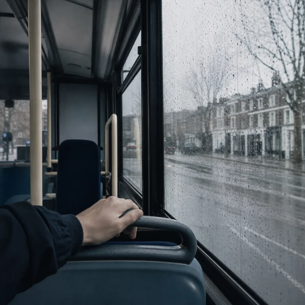 The inside of a London bus on a grey afternoon, a hand on the rail and rain running down the window.